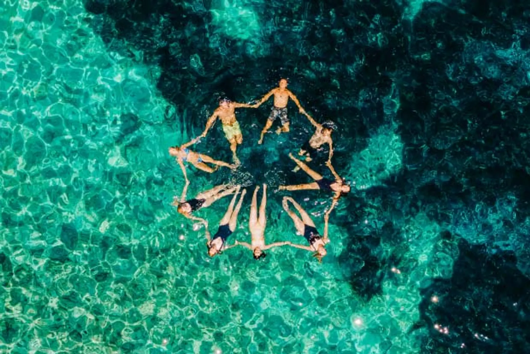 Image of friends in a star formation floating together in clear blue water