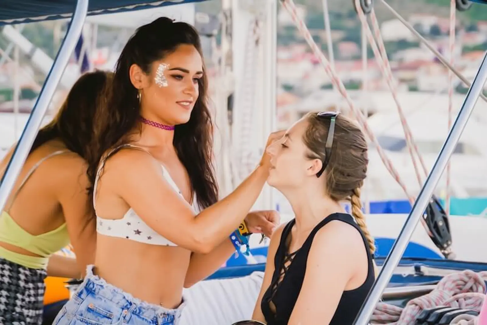 A woman putting glitter and face makeup on another woman for a European summer music festival while they sail Croatia.